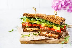 Vegan sandwich with tofu, hummus, avocado, tomato and sprouts