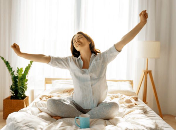 Happy woman enjoys morning coffee in the bedroom with houseplant