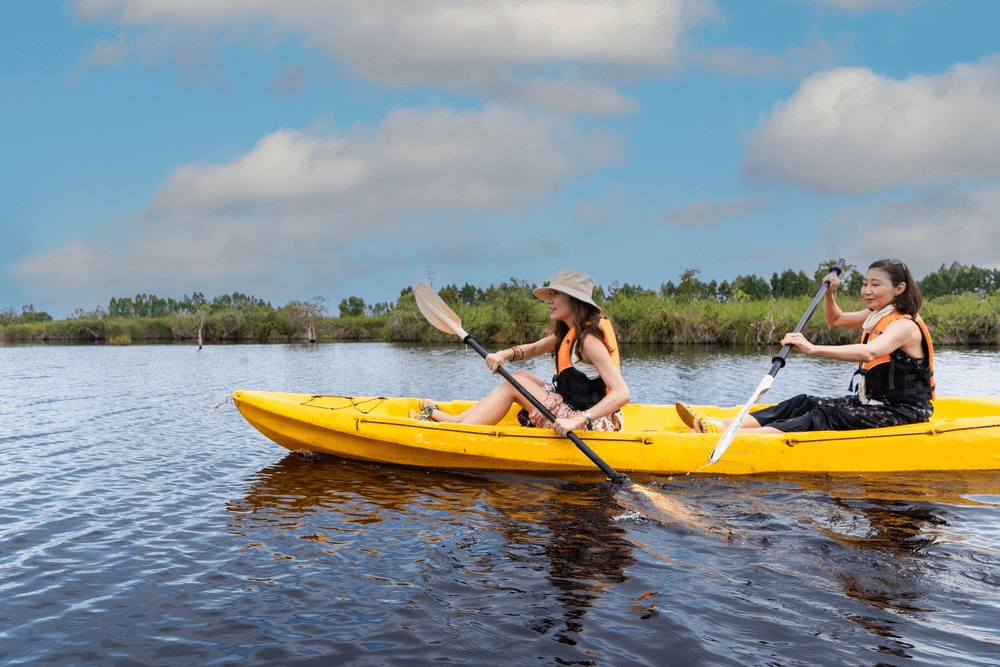 Two people paddling a tandem kayak on a lake with a longer paddle